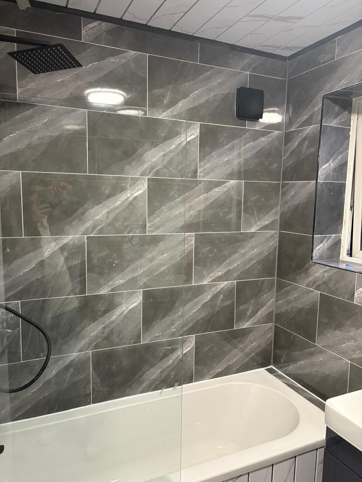 Grey marble-effect tiling, bath and black rainfall shower fitted by CH Developments in Birmingham