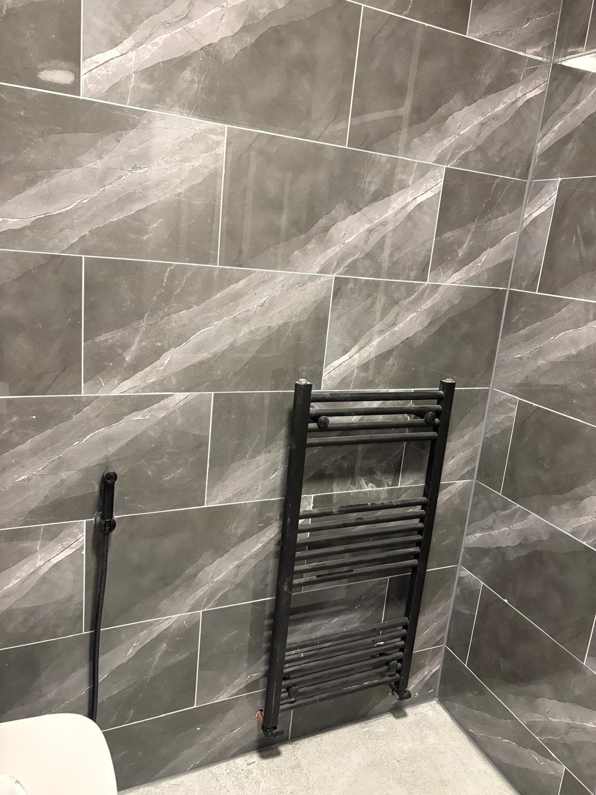 Grey marble-effect bathroom tiling with black ladder towel radiator by CH Developments in Birmingham